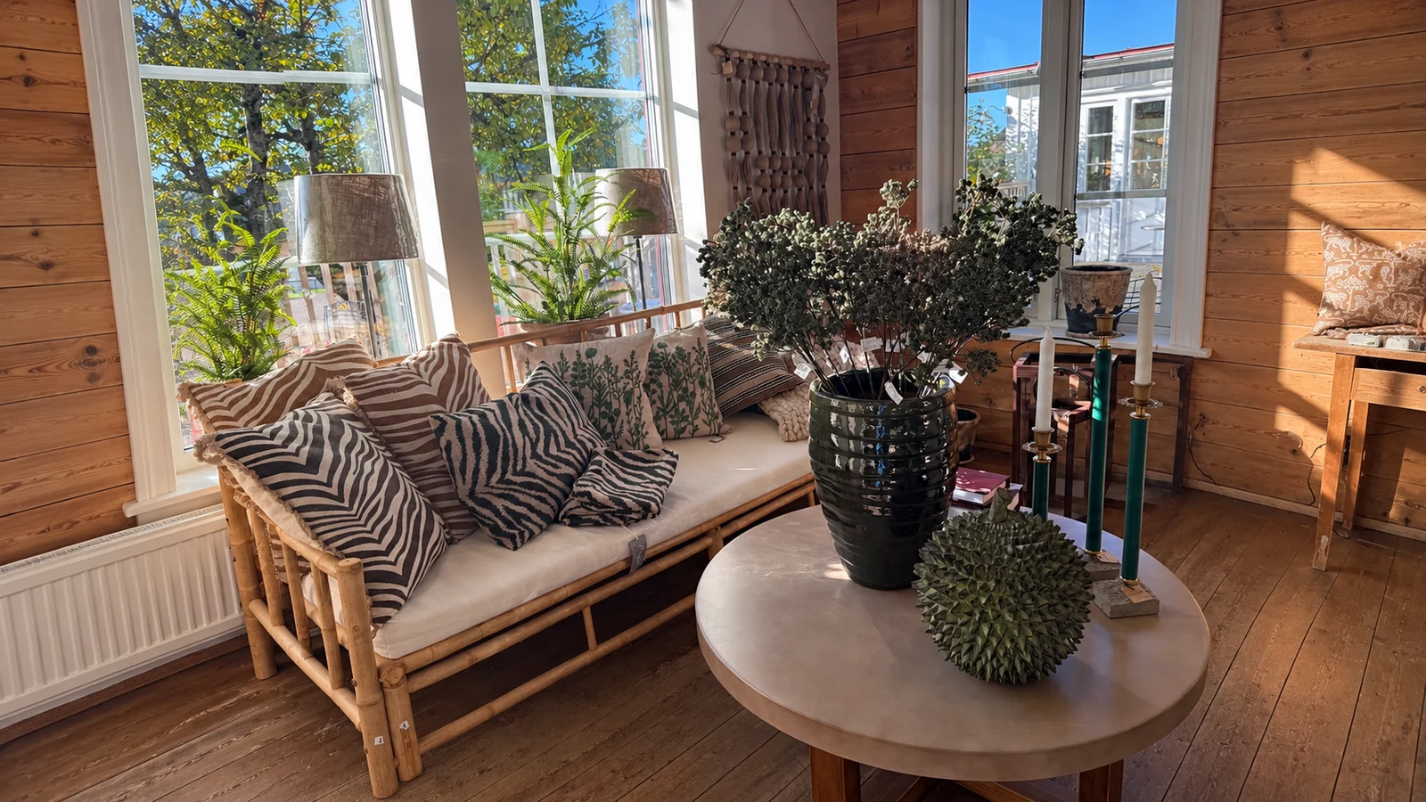Lantlig butiksmiljö med kuddar, soffa, keramik och solljus genom fönstren